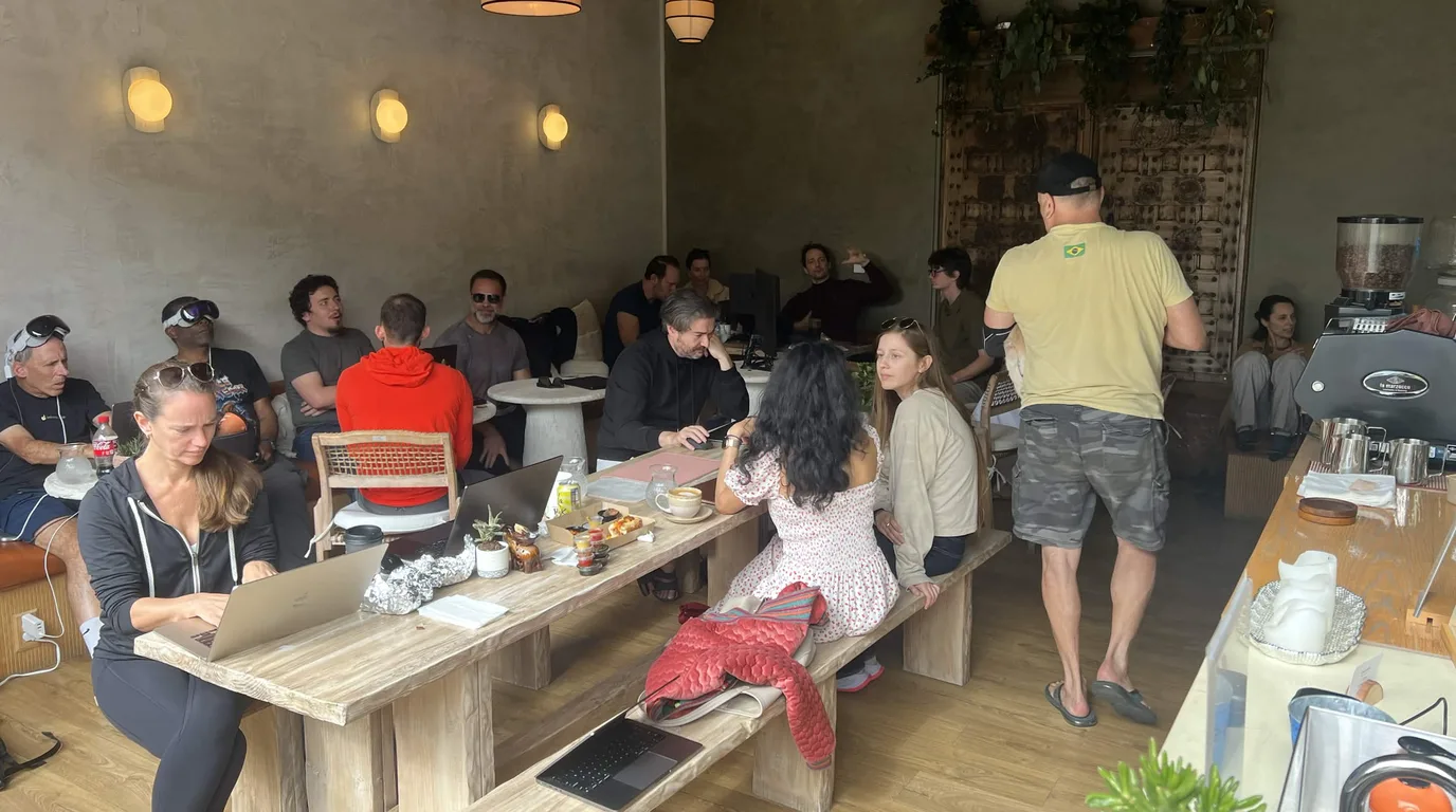 A Science Sunday session under way in the Venice café — around a dozen people along a long communal table with laptops, notebooks and coffee, two of them wearing headsets pushed up on their foreheads, under warm pendant lamps